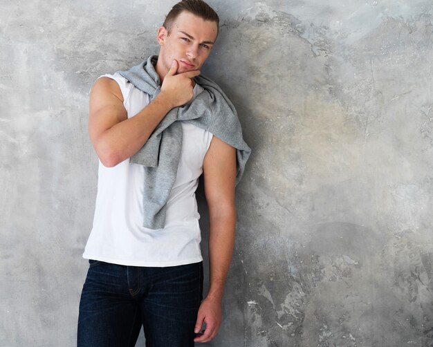 Portrait d'un beau jeune homme, mannequin. Posant sur un mur gris.