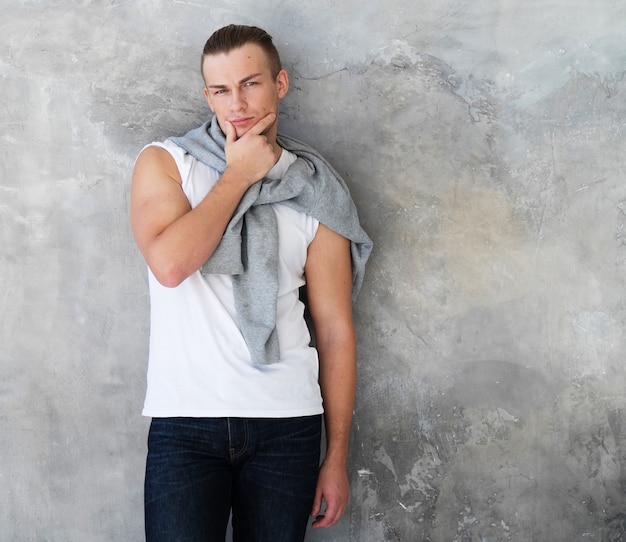 Portrait d'un beau jeune homme, mannequin. Posant sur un mur gris.