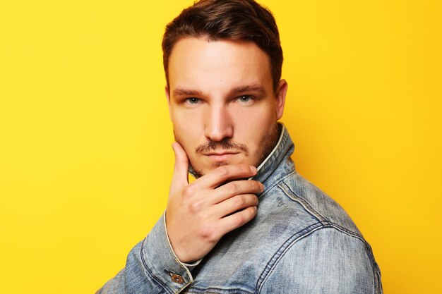 Portrait d'un beau jeune homme mannequin posant sur un mur jaune Concept de style de vie et de mode