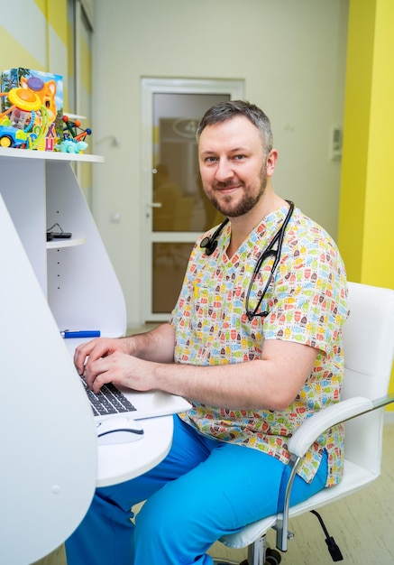 Portrait d'un beau jeune homme médecin souriant avec stéthoscope autour du cou portant un uniforme brillant dans une armoire médicale