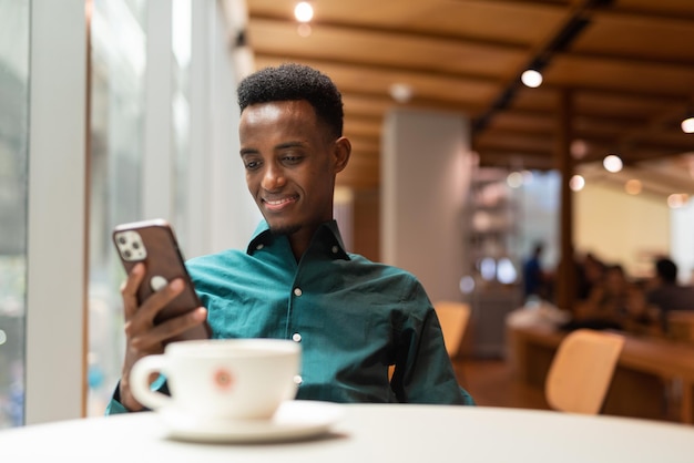 Portrait de beau jeune homme noir dans un café à l'aide de téléphone