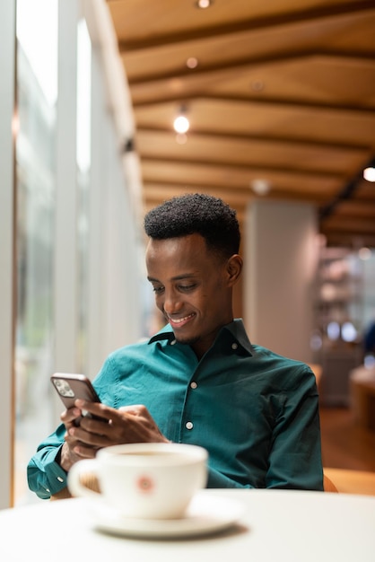 Portrait de beau jeune homme noir dans un café à l'aide de téléphone