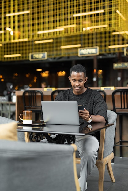 Portrait d'un beau jeune homme noir utilisant un ordinateur portable dans un café