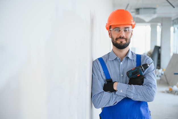 Portrait d'un beau jeune homme positif en casque tout en travaillant sur un chantier de construction