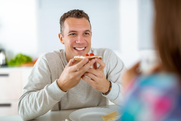 Portrait d'un beau jeune homme qui mange un sandwich sain pour le petit déjeuner dans la cuisine domestique.