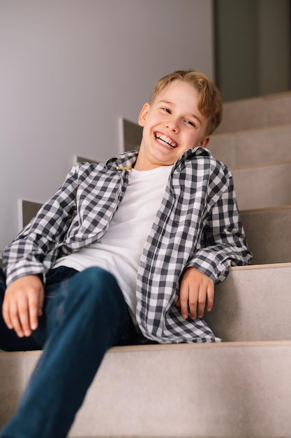 Portrait d'un beau jeune homme riant jeune adolescent assis sur les marches à l'intérieur