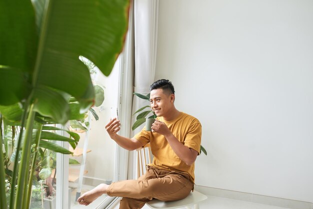 Portrait de beau jeune homme avec smartphone près de la fenêtre