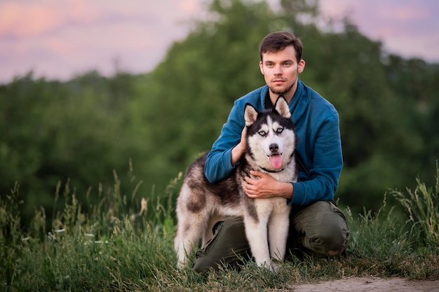 Portrait d'un beau jeune homme et de son chien Husky sibérien dans la nature en soirée au coucher du soleil