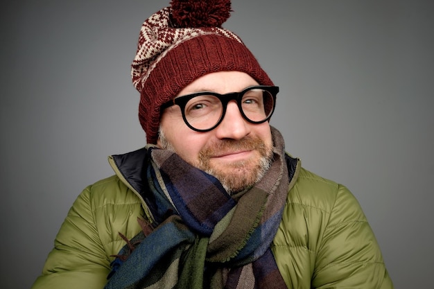 Portrait d'un beau jeune homme souriant portant une écharpe de manteau d'hiver chaud et un chapeau drôle