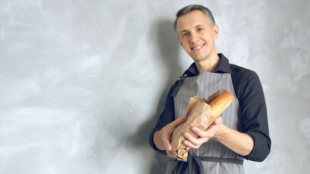 Photo portrait d'un beau jeune homme en uniforme tenant de délicieuses baguettes fraîches sur un fond gris.