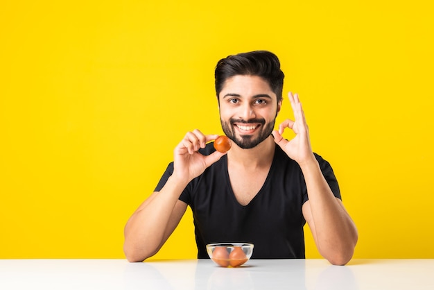 Portrait d'un beau jeune indien manÃ‚Â manger sweet Gulab Jamun sur fond jaune