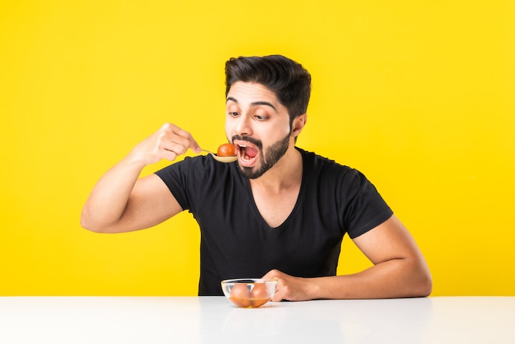 Photo portrait d'un beau jeune indien manã‚â manger sweet gulab jamun sur fond jaune