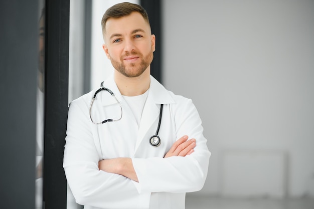 Portrait d'un beau jeune médecin dans le couloir de l'hôpital regardant la caméra en souriant