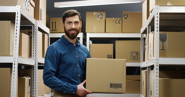 Portrait de beau jeune messager, souriant joyeusement à la caméra au bureau de poste