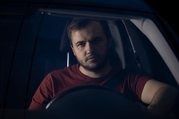 Portrait de beau jeune pilote millénaire est assis au volant de voiture de nuit pensivement à l'avant