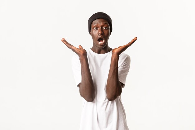 Portrait de beau mâle afro-américain surpris et confus, bouche ouverte et mains étendues sur le côté