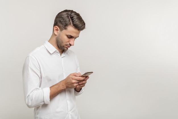 Portrait d'un beau mec curieux portant des envois occasionnels et recevant des messages isolés sur blanc