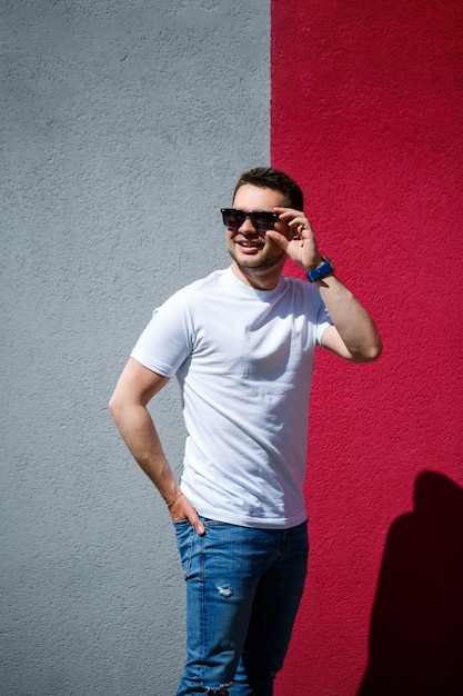 Portrait d'un beau mec élégant, un homme vêtu d'un t-shirt blanc vierge debout sur un fond de mur gris et rouge. Style urbain de vêtements, image à la mode moderne. La mode masculine