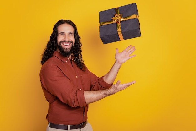 Portrait de beau mec funky positif attraper un sourire à pleines dents boîte-cadeau sur fond jaune