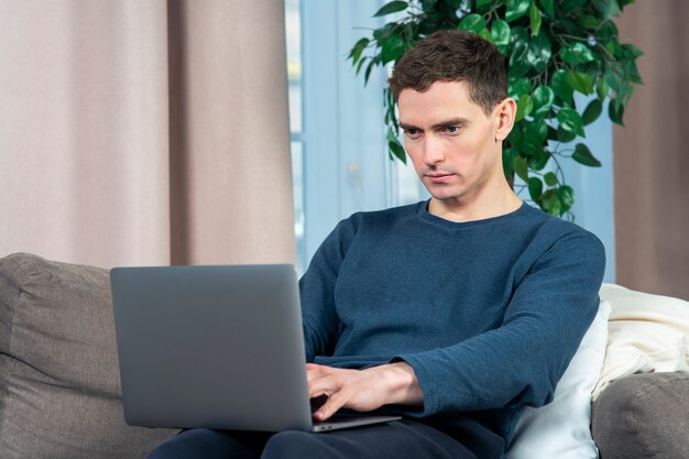 Portrait de beau mec jeune homme pigiste travaille sur son ordinateur portable sur un canapé ou un canapé à