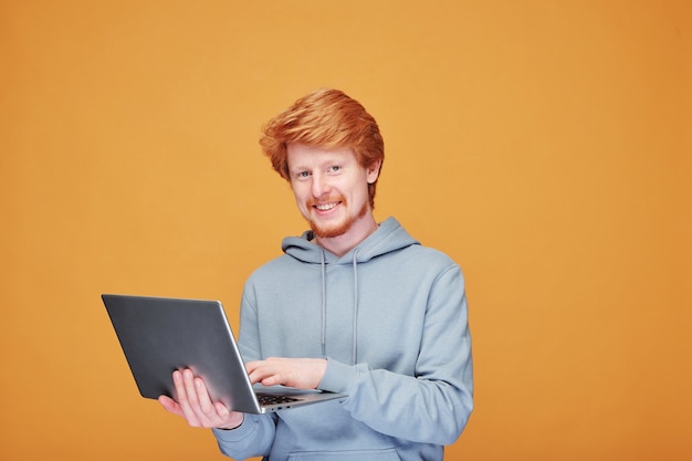 Portrait d'un beau mec rousse souriant faisant des gestes de côté tout en présentant un nouveau produit contre le mur orange