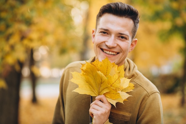 Portrait de beau mec souriant et tenant un bouquet de feuilles d'automne dans le parc