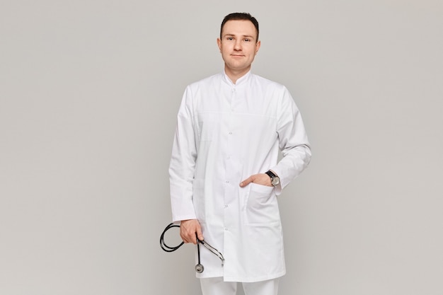 Portrait De Beau Médecin Posant En Uniforme Médical Avec Stéthoscope Sur Fond Gris.