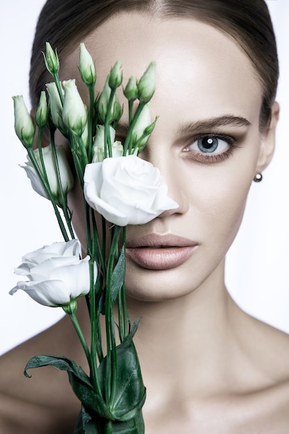 Portrait de beau modèle avec une bonne peau sur fond blanc avec fleur de roses blanches.