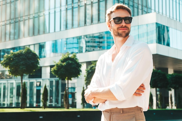 Portrait de beau modèle sexuel hipster élégant et souriant Homme moderne vêtu d'une chemise blanche Homme de mode posant dans le fond de la rue près des gratte-ciel à lunettes