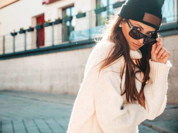 Portrait de beau modèle souriant. Femme vêtue d'un pull blanc et d'un bonnet chauds. Femme à la mode posant dans la rue