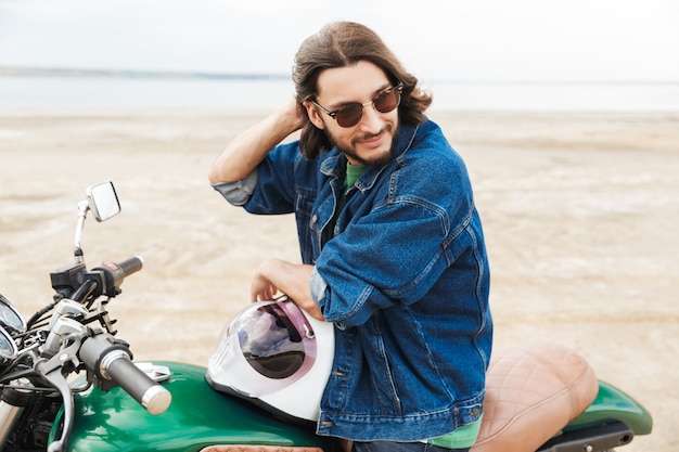 Portrait d'un beau motard heureux homme optimiste positif sur son vélo à l'extérieur sur une plage.