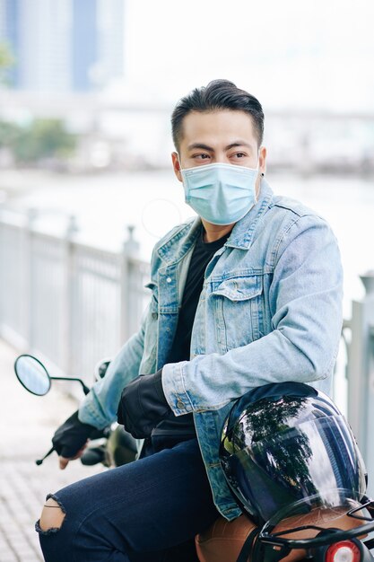 Portrait de beau motocycliste en masque médical assis sur le vélo et à l'écart