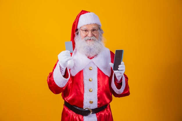 Portrait d'un beau père Noël tenant une carte de crédit et un smartphone avec un écran vide pour le texte dans sa main.