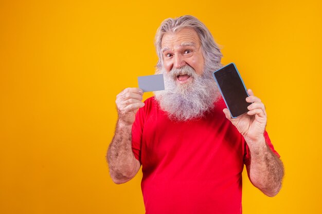 Portrait d'un beau père Noël tenant une carte de crédit et un smartphone avec un écran vide pour le texte dans sa main.