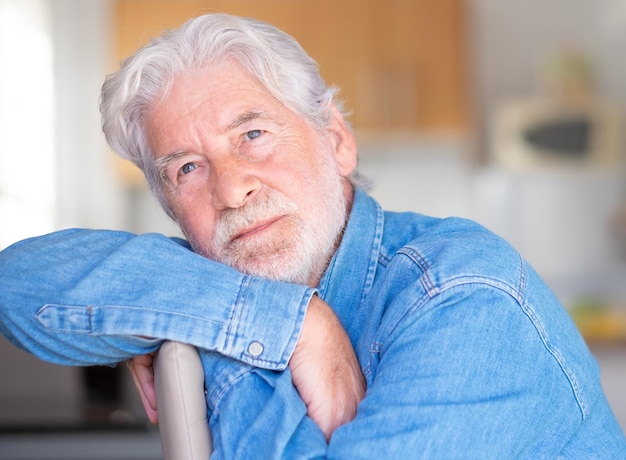 Portrait d'un beau senior adulte avec barbe assis à la maison regardant pensivement