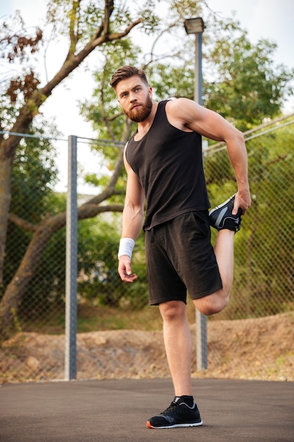 Portrait d'un beau sportif barbu qui s'étend des jambes à l'extérieur