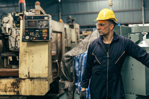 Portrait beau travailleur avec combinaison de sécurité et vieille machine en usine.