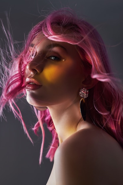 Portrait de beauté art d'une femme aux cheveux roses, coloration créative. Des reflets aux couleurs vives et des ombres sur le visage, une fille avec des bijoux. Cheveux teints au vent