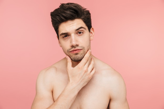 Portrait de beauté d'un bel homme brune torse nu confiant, debout isolé sur un mur rose, regardant la caméra