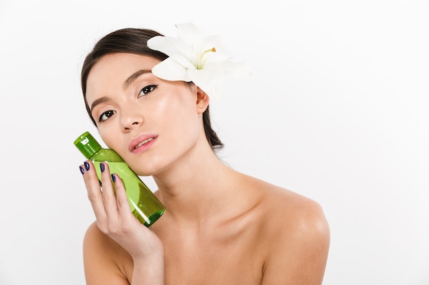 Portrait de beauté de belle femme asiatique avec une fleur dans les cheveux tenant une lotion pour le corps ou de l'huile de spa à la main, isolé sur blanc