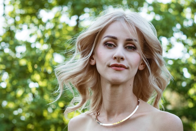 Portrait de beauté d'une belle femme blonde avec un collier sur un fond vert naturel