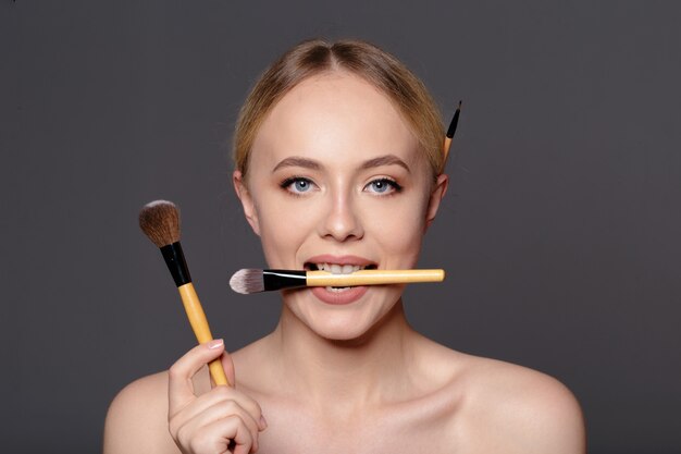 Portrait de beauté d'une belle femme à moitié nue souriante posant avec des pinceaux à maquillage