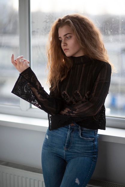 Photo portrait de beauté d'une belle jeune femme aux cheveux bouclés portant une valise noire et un jean posant près de fenêtres lumineuses