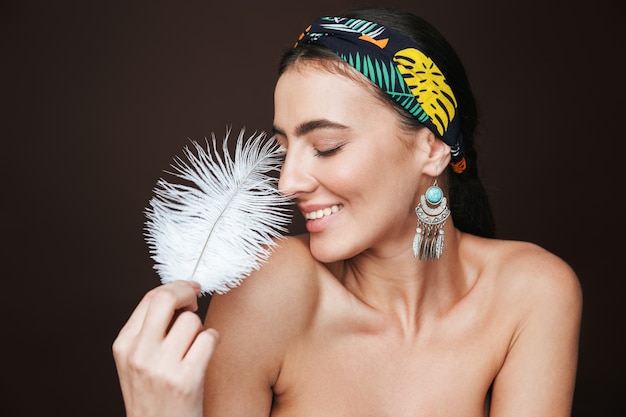 Portrait de beauté d'une belle jeune femme aux seins nus portant un bandeau et des boucles d'oreilles debout isolé sur noir