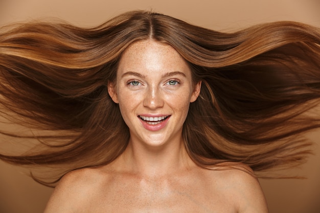 Portrait de beauté d'une belle jeune femme en bonne santé avec de longs cheveux rouges regardant la caméra isolée sur mur beige