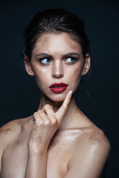 Portrait de beauté d'une belle jeune femme pensive avec un maquillage chatoyant sur une surface noire