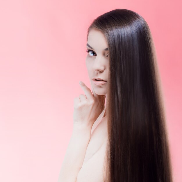 Portrait de beauté brune avec des cheveux parfaits, sur un mur rose. Soin des cheveux