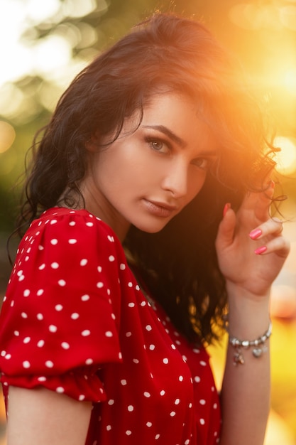 Portrait de beauté d'été d'une belle femme bouclée avec un bracelet de mode en robe rouge rétro se promène au coucher du soleil