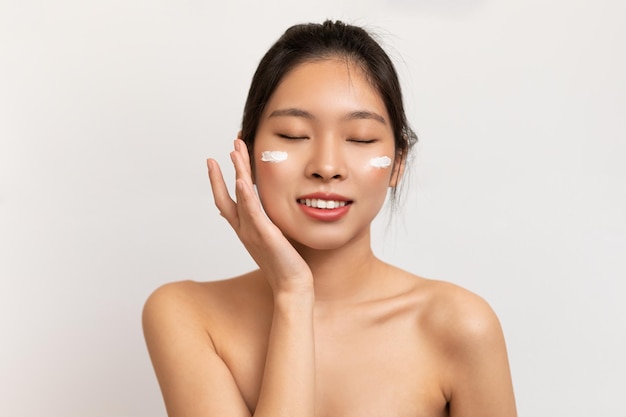 Portrait de beauté d'une femme asiatique touchant l'application de crème sur la joue