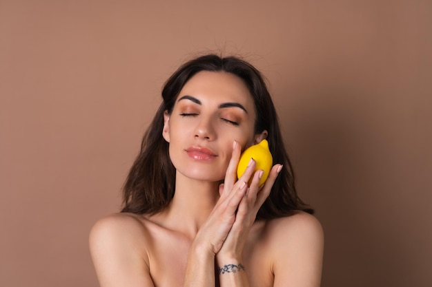 Photo portrait de beauté d'une femme aux seins nus avec une peau parfaite et un maquillage naturel sur fond beige contient des vitamines c citron citron pour la peau